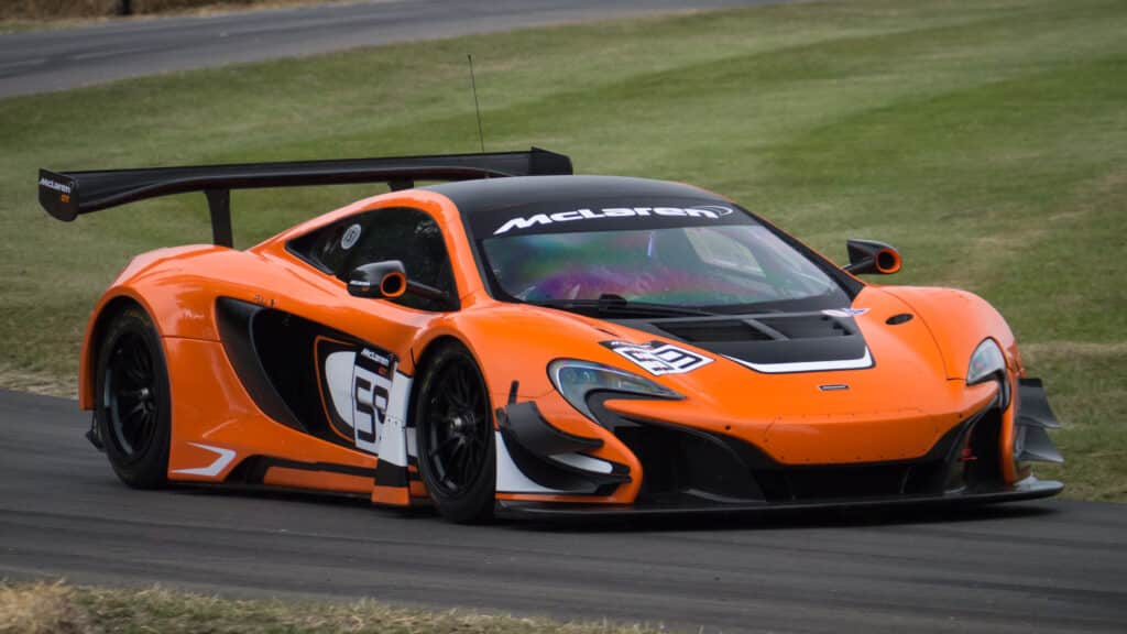 Un coche deportivo McLaren P1 en color naranja con detalles en negro, con el número ‘59’ en el lateral y el logotipo de McLaren en el alerón trasero. El vehículo está posicionado en lo que parece ser una pista de carreras, sugiriendo rendimiento y velocidad como puntos de interés.