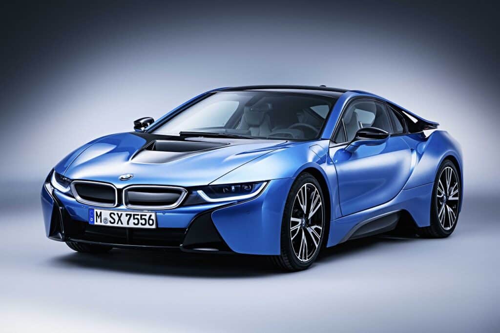 Coche deportivo BMW i8 azul con puertas de tijera, resaltando su diseño aerodinámico y futurista. El vehículo está posicionado en un ángulo que destaca su perfil bajo y elegante, con un fondo neutro que acentúa su vibrante color y tecnología avanzada.