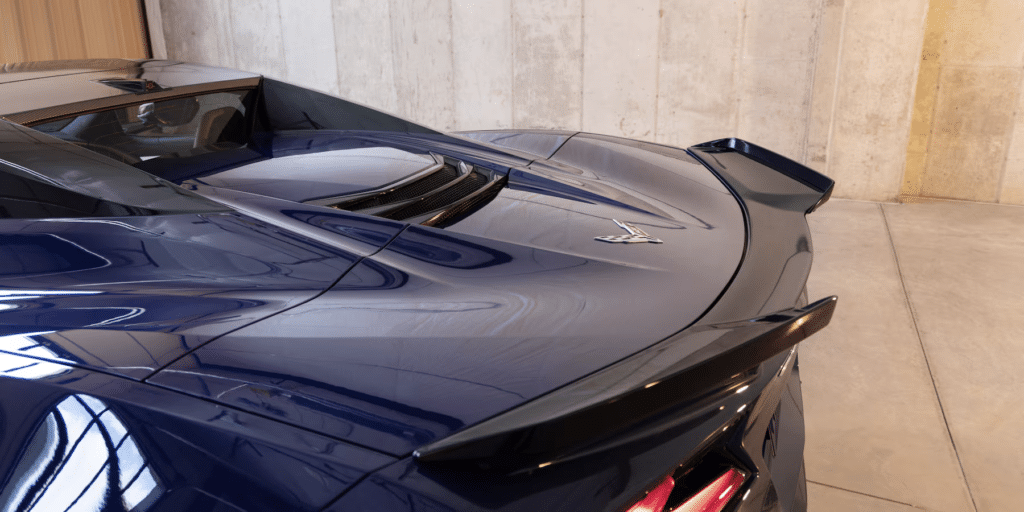 Imagen de la parte trasera de un Corvette ZR1 2025 azul, destacando las luces traseras distintivas, el alerón trasero y las insignias específicas del modelo ZR1. El coche está estacionado dentro de un edificio con paredes de concreto, lo que sugiere que podría estar en una sala de exposición o garaje. Los elementos de diseño, como las líneas elegantes y los contornos aerodinámicos, resaltan la naturaleza orientada al rendimiento de este modelo deportivo.