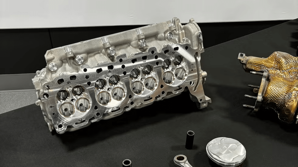 Culata y válvulas del motor LT7 del Corvette ZR1. La culata, hecha de aluminio, presenta múltiples aberturas circulares para las válvulas y las bujías. También se observan pasajes para el refrigerante o el aceite. Este componente es crucial para el rendimiento del motor, ya que alberga las válvulas de admisión y escape, que controlan el flujo de aire y gases de escape en los cilindros. La culata del LT7 está diseñada para soportar altas temperaturas y presiones, optimizando la eficiencia y potencia del motor.