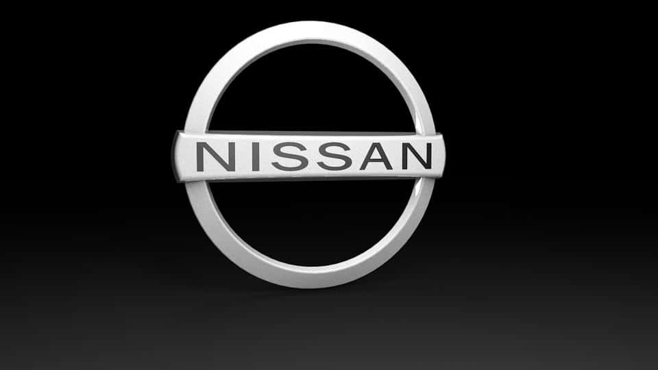 Renderizado 3D de una pieza de recambio para un vehículo, específicamente el logotipo de Nissan. El logotipo consiste en un círculo plateado con una barra horizontal en el centro, mostrando la palabra ‘NISSAN’ en mayúsculas. El fondo es oscuro, resaltando el acabado metálico y el aspecto tridimensional del logotipo. piezas de coche impresora 3d