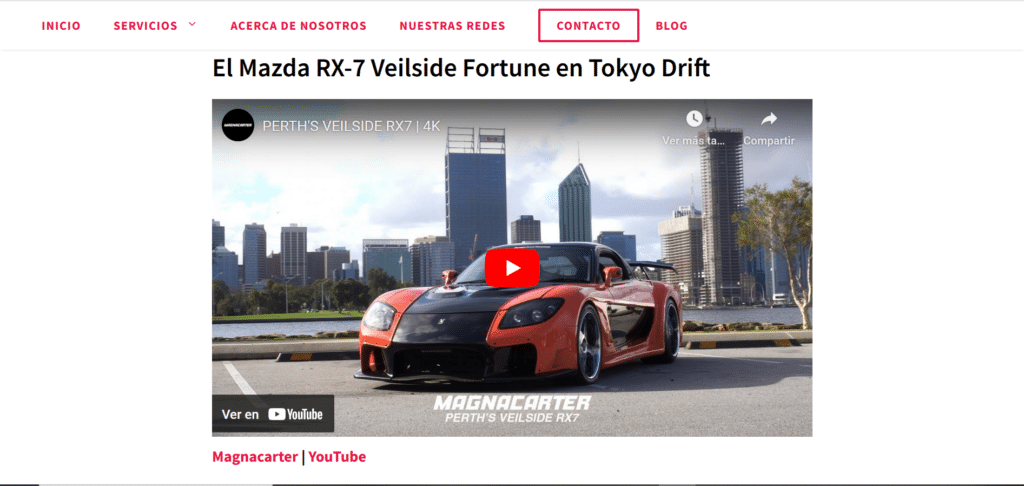 Una página web con una barra de navegación en la parte superior que contiene opciones como “INICIO,” “SERVICIOS,” “ACERCA DE NOSOTROS,” “NUESTRAS REDES,” “CONTACTO,” y “BLOG.” Debajo de la barra de navegación, hay una imagen grande de un Mazda RX-7 rojo con la leyenda “El Mazda RX-7 Veilside Fortune en Tokyo Drift” y un botón de reproducción que indica que es una miniatura de video. El fondo de la miniatura presenta rascacielos, sugiriendo un entorno urbano. La imagen sugiere el uso de “Redacción SEO para sitios web de automóviles” en el contexto de contenido visual y multimedia relacionado con automóviles.