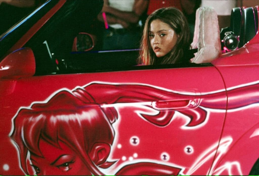 Devon Aoki en un Honda S2000 rosa con un gráfico de un personaje animado femenino con cabello suelto en el lateral. La imagen está asociada con la película ‘2 Fast 2 Furious’.
