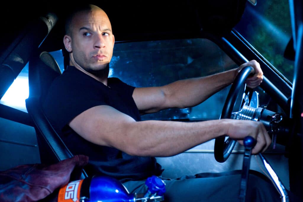 Imagen del interior del Dodge Charger R/T de 1970 de Dominic Toretto en la película ‘The Fast and the Furious’. Se puede ver a Toretto, interpretado por Vin Diesel, conduciendo el coche. El volante y el tablero de instrumentos son visibles, con detalles en cromo y un diseño clásico de muscle car.