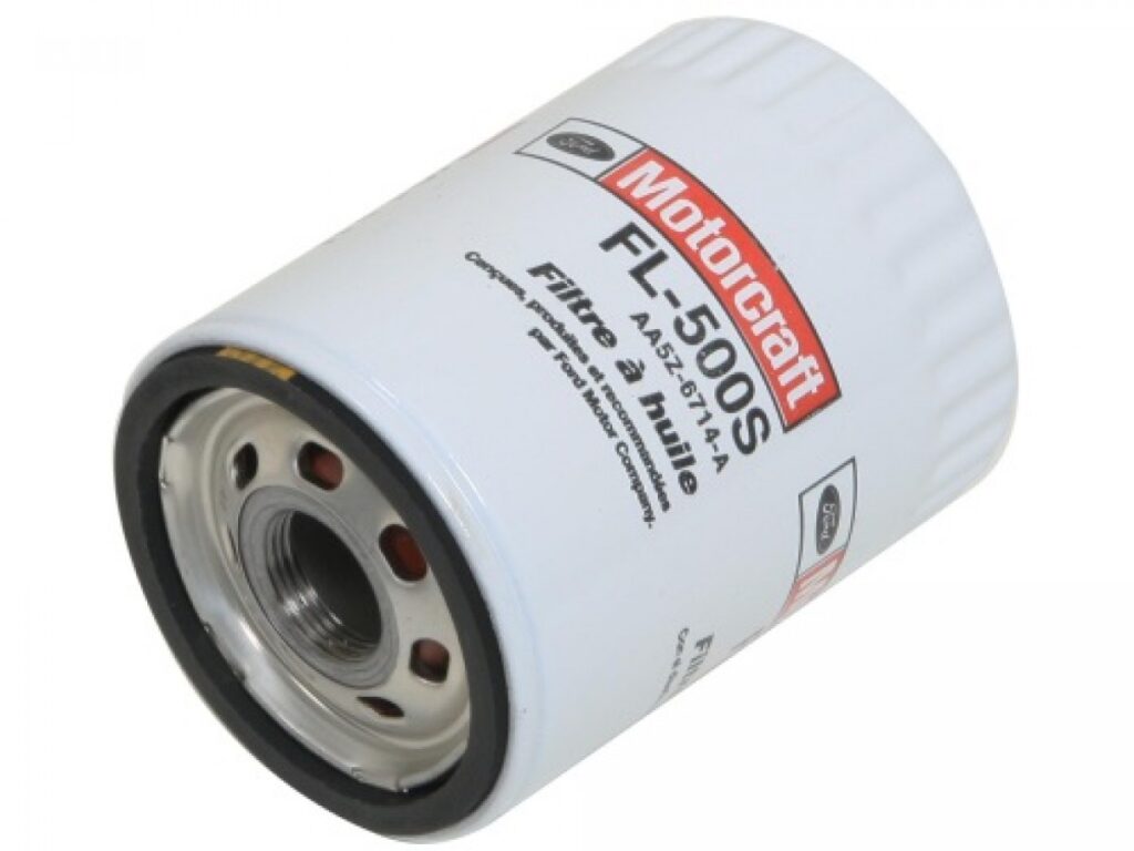 Imagen de un filtro de aceite Motorcraft modelo FL-500S. El filtro es cilíndrico, predominantemente blanco con un anillo rojo en el extremo abierto, y tiene texto y logotipos impresos en su lateral. Este componente es esencial para el mantenimiento del vehículo, ya que filtra los contaminantes del aceite del motor. Es importante asegurarse de que el filtro esté correctamente instalado y que el coche esté levantado de manera segura desde los refuerzos de la carrocería o el chasis en el caso de todoterrenos y furgonetas.