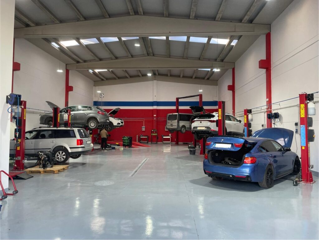 HTM GARAJE: nuevo alquiler de boxes en Zaragoza, donde cambiar el aceite del coche uno mismo. Interior de un taller mecánico diseñado para el alquiler de boxes, permitiendo a las personas realizar el mantenimiento de sus coches. Se observan coches en elevadores, herramientas y equipos especializados, dentro de un ambiente amplio y bien iluminado.