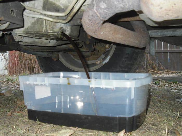 Imagen de la parte inferior de un coche con aceite siendo drenado del motor hacia un recipiente de plástico transparente. Este proceso es parte del cambio de aceite, una tarea de mantenimiento rutinaria para asegurar el buen funcionamiento del motor.