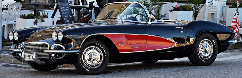 Redactor automotriz: Imagen de un Chevrolet Corvette C1 clásico bicolor, predominantemente negro con una sección roja en el lateral, estacionado en una calle. El vehículo parece ser un modelo vintage o retro, posiblemente de mediados del siglo XX, y es interesante debido a su diseño distintivo y la nostalgia que evoca por el estilo automotriz clásico.