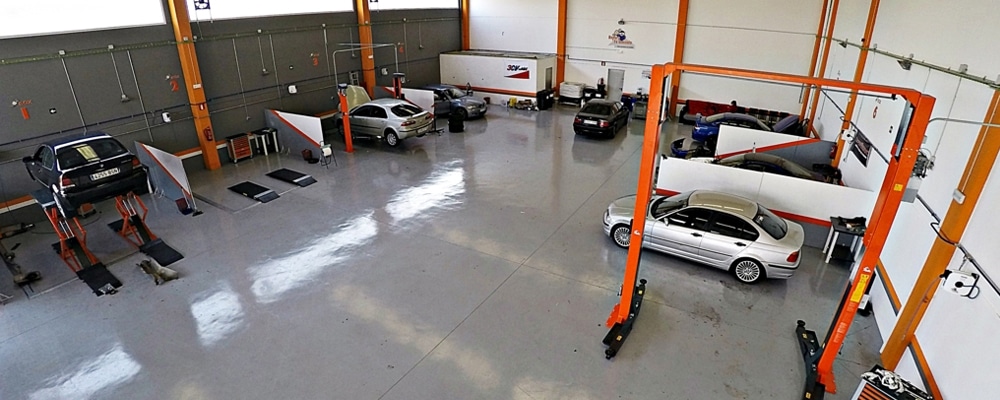 Donde cambiar el aceite del coche uno mismo en Bilbao: Imagen de un amplio taller de reparación de vehículos. Hay varios elevadores de coches con vehículos sobre ellos, y el taller está equipado con diversas herramientas y maquinaria probablemente utilizadas para el mantenimiento y reparación de vehículos. La imagen muestra un entorno adecuado para realizar el cambio de aceite del coche uno mismo, sugiriendo que es un taller de autoservicio o tipo ‘hazlo tú mismo’ en Bilbao.