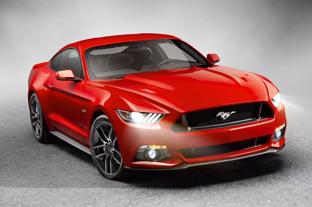 Ford Mustang 2015 en rojo, mostrado en un ángulo que destaca su diseño elegante con una parrilla frontal prominente que presenta el emblema del Mustang. El vehículo está colocado contra un fondo gris degradado que resalta su color vibrante y estética deportiva.