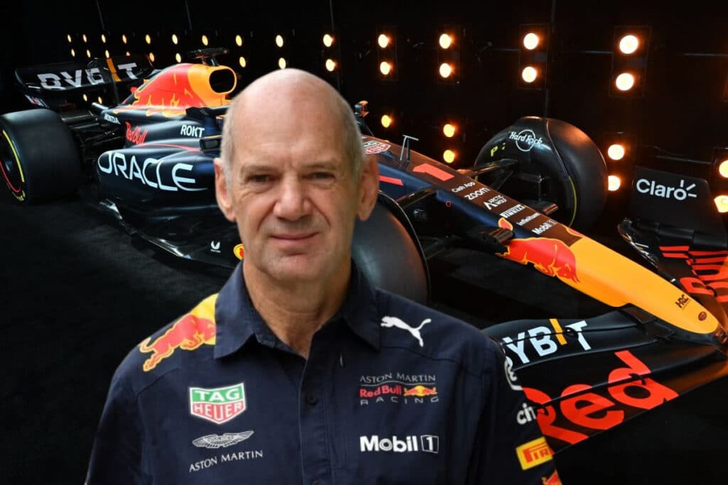 La imagen muestra a Adrian Newey frente a un coche de Fórmula 1 de Red Bull Racing. El coche presenta marcas prominentes de patrocinadores como Oracle, Mobil 1, TAG Heuer y Aston Martin. El fondo incluye una serie de luces que dan la impresión de velocidad o movimiento. Esta imagen es relevante para mostrar el diseño y los detalles de patrocinio de un coche de Fórmula 1 de Red Bull Racing, lo cual puede ser de interés para los aficionados al automovilismo o aquellos que estudian el branding en deportes.