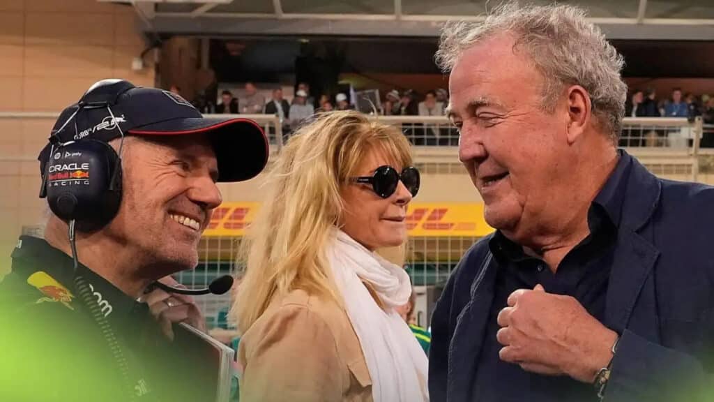 Adrian Newey, con gorra y auricular, y Jeremy Clarkson comparten una broma en la parrilla de salida del Gran Premio de Bahréin 2024. Newey, conocido ingeniero de Fórmula 1, y Clarkson, famoso presentador de televisión, están en un evento al aire libre, con barreras y otros elementos típicos de un Gran Premio de Fórmula 1 visibles en el fondo.