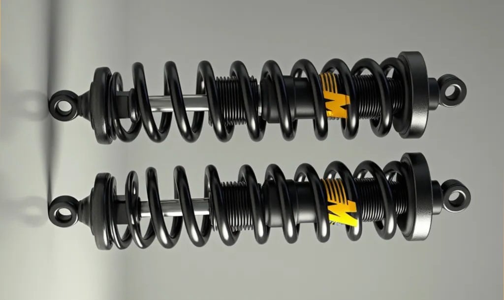 La imagen muestra un par de amortiguadores para el sistema de suspensión de un vehículo. Estos componentes son cruciales para asegurar un viaje suave al absorber y amortiguar el impacto de la carretera. Cada amortiguador tiene un resorte en espiral alrededor, con marcas amarillas visibles en parte de los resortes, lo que podría indicar una marca o tipo específico de resorte.