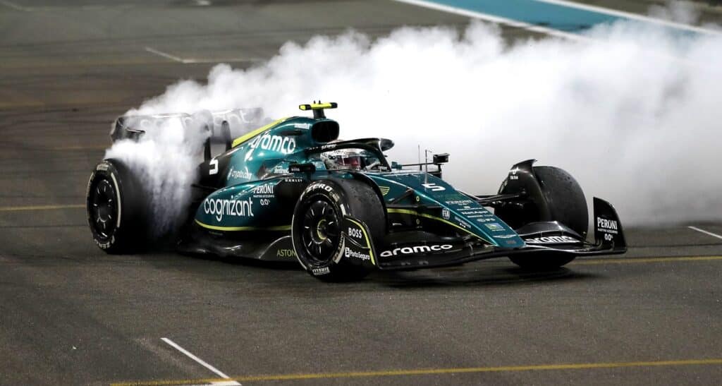 La imagen muestra un coche de carreras de Fórmula 1 de Aston Martin en una pista, emitiendo una gran cantidad de humo blanco desde la parte trasera mientras realiza trompos. El coche es predominantemente verde oscuro con logotipos de patrocinadores, incluyendo “Cognizant” y “Aramco”. El número ‘3’ es visible en la parte delantera del coche. Esta imagen captura un momento dinámico y emocionante durante una sesión de trompos.