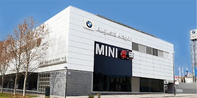 Imagen de un edificio moderno con una gran fachada que incluye los logotipos de BMW y MINI. El nombre “BMW Augusta Aragón” está claramente visible en el edificio, indicando que es probablemente un concesionario o edificio corporativo asociado con la marca BMW.