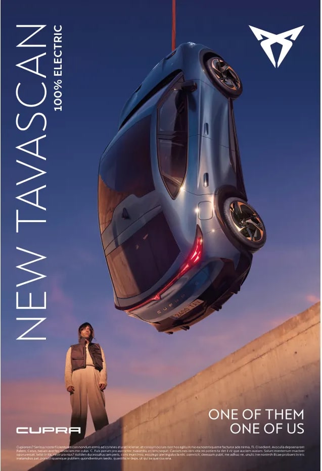 Anuncio del ‘NEW TAVASCAN - 100% ELECTRIC’ de CUPRA. La imagen muestra un coche suspendido en el aire en ángulo, con la parte delantera hacia abajo y la trasera hacia arriba, contra un cielo despejado. Debajo del coche, hay una persona de pie sobre una superficie inclinada, vestida con un atuendo que coincide con la estética del vehículo. El texto en la parte inferior dice ‘ONE OF THEM ONE OF US’.