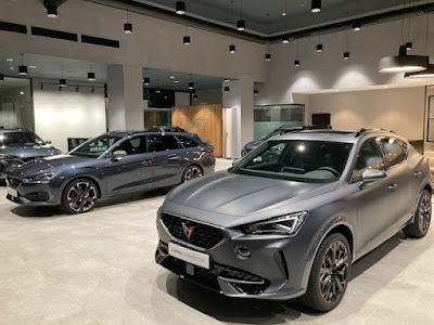 Imagen del interior de un showroom con tres vehículos de la marca Cupra en exhibición. El showroom tiene un diseño moderno y elegante, con una paleta de colores predominantemente gris que combina con la estética de los vehículos.