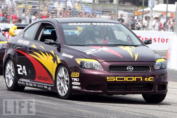 Keanu Reeves compitiendo en el Toyota Grand Prix Pro/Celebrity Race Day el 17 de abril de 2010 en Long Beach, California. Conduce un coche de carreras SCION tC oscuro con el número 24 y un diseño de llamas rojas, amarillas y naranjas en los laterales.