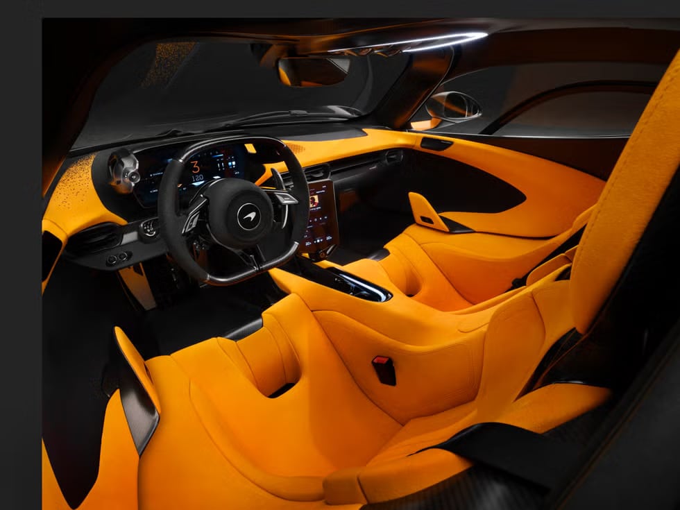 Interior de un McLaren W1 de lujo, con un volante que lleva el emblema de McLaren en el centro. El tablero y los asientos están tapizados en un vibrante color amarillo con detalles y acabados en negro. El diseño es moderno y elegante, indicando un modelo de coche deportivo de alta gama.