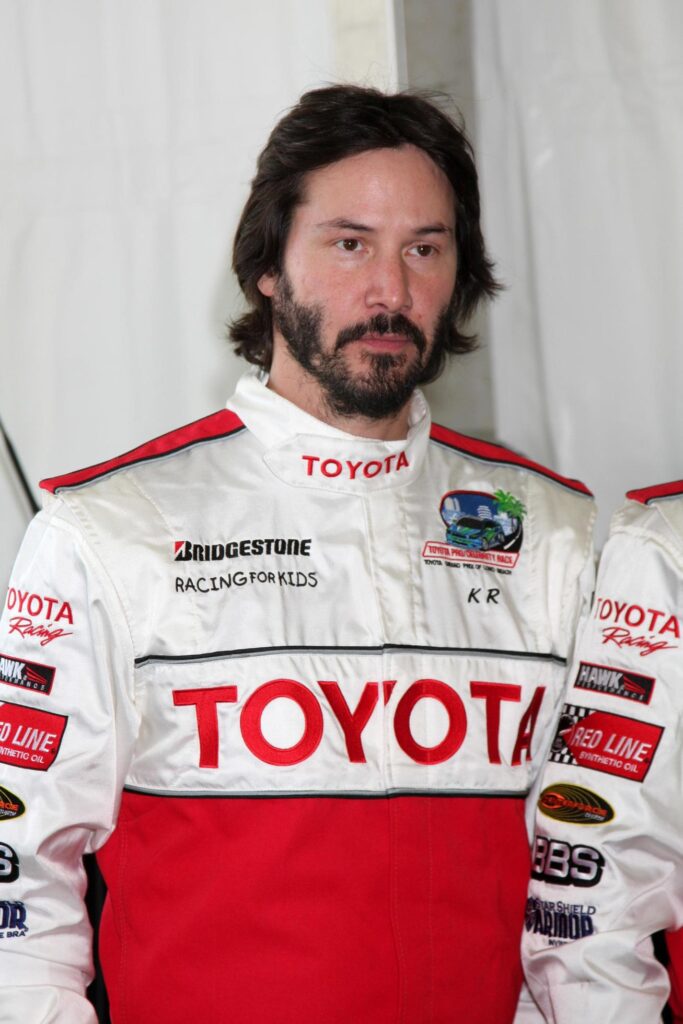 Keanu Reeves en el 33º día de prensa anual de la carrera Toyota Pro/Celebrity en la pista del Gran Premio en Long Beach, California, el 7 de abril de 2009. Lleva un traje de carreras rojo y blanco con varios logotipos de marcas automotrices.