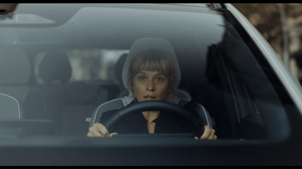 La imagen muestra a una mujer rubia conduciendo un coche Volvo. Su rostro refleja sorpresa y alivio, ya que el sistema de frenado automático del coche se ha activado para evitar un atropello. La escena destaca la importancia del sistema de detección de peatones del Volvo, que ha protegido a la futura mamá.