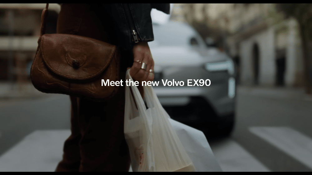 La imagen muestra una bolsa de compras en la mano de una mujer embarazada, con un coche Volvo detenido cerca. La escena sugiere que el coche ha frenado de repente, evitando un posible accidente. La bolsa de compras en la mano de la mujer indica que estaba cruzando la calle cuando el coche se detuvo. Esta imagen destaca la eficacia del sistema de detección de peatones del Volvo, que ha evitado un atropello