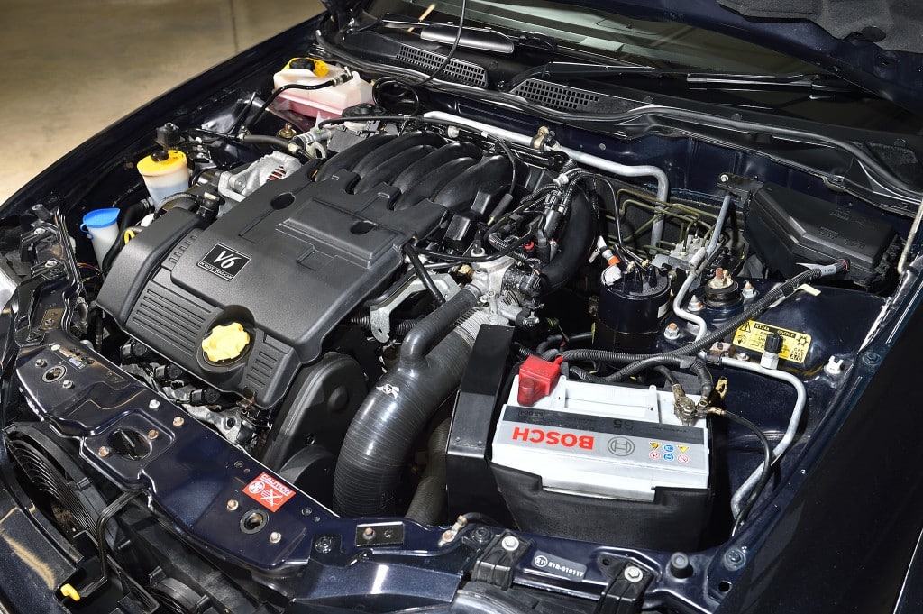 "La imagen muestra el compartimento del motor de un coche MG ZS 180. El motor es un V6, como indica la etiqueta en la cubierta del motor. La batería es de la marca Bosch, y se pueden ver varios componentes como el depósito de refrigerante, la tapa del aceite y otras partes del motor. Esta imagen es interesante y relevante porque proporciona una vista detallada de la disposición y los componentes del motor, lo cual puede ser útil para entender la configuración mecánica del coche o para realizar mantenimiento.