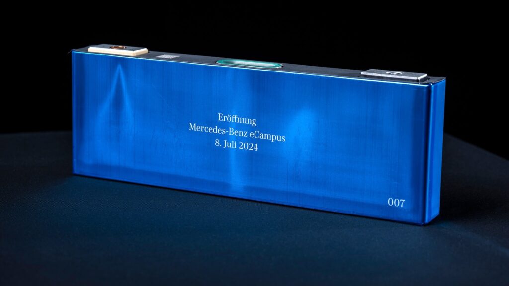 Una batería azul rectangular con texto impreso que dice: 'Eröffnung Mercedes-Benz eCampus 8. Juli 2024'. En la esquina inferior derecha, hay un número '007'. Esta imagen parece ser una celda de batería o un componente similar, relacionado con la inauguración del eCampus de Mercedes-Benz el 8 de julio de 2024.