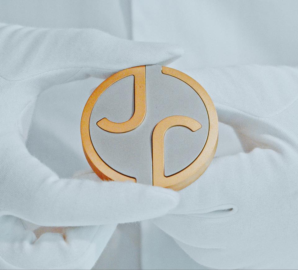 La imagen muestra el nuevo logo de Jaguar, que consiste en un diseño circular metálico con formas estilizadas que parecen las letras 'J' y 'P'. El borde exterior es de color dorado, mientras que la parte interior es plateada o gris. Aunque el logo intenta transmitir modernidad y sofisticación, su ejecución deja mucho que desear. La combinación de colores y formas no logra capturar la esencia de la marca Jaguar, conocida por su elegancia y dinamismo. En lugar de evocar la imagen de un felino ágil y poderoso, este logo parece más una mezcla confusa de elementos sin una identidad clara. En resumen, este diseño no está a la altura de la reputación de Jaguar y podría considerarse un intento fallido de renovación.