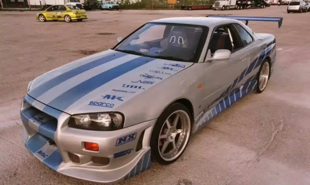 El espectacular Nissan Skyline R34 GT-R de la película "2Fast 2 Furious", con su pintura plateada y las franjas azules estilo muscle cruzando el coche a lo largo.