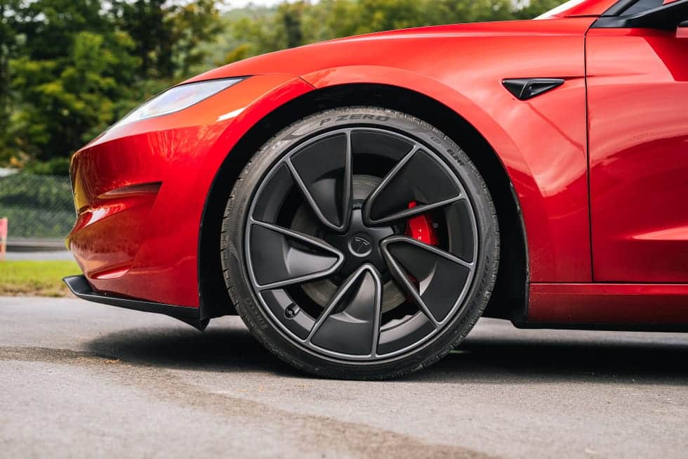 Claro, aquí tienes: La imagen muestra la rueda delantera izquierda de un coche rojo, específicamente un Tesla. La rueda tiene un diseño de llanta negra con múltiples radios y un cáliper de freno rojo visible. El neumático es un Pirelli P Zero, como indica el texto en el neumático. El diseño elegante del coche y los componentes de alto rendimiento del neumático y el freno sugieren que se trata de un vehículo de alto rendimiento, probablemente un Tesla Model S Plaid. La imagen es interesante porque destaca los elementos avanzados de ingeniería y diseño del coche, que son puntos clave de venta para los vehículos eléctricos de alto rendimiento.