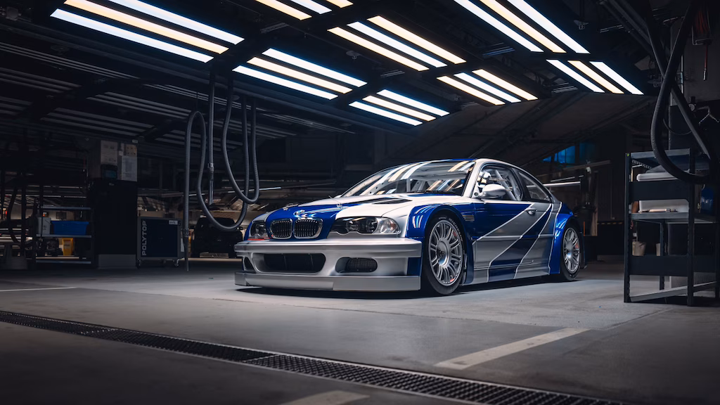 Ahora para esta del BMW M3 GTR de Need for Speed Most Wanted. No omitas esos detalles:
La imagen muestra un BMW M3 GTR, un coche de carreras de alto rendimiento, estacionado en un garaje o taller bien iluminado. El coche presenta una distintiva librea azul y blanca con calcomanías de carreras, un kit de carrocería ancho y mejoras aerodinámicas, lo que lo hace visualmente llamativo. Este coche es particularmente interesante y relevante porque es famoso por el videojuego "Need for Speed: Most Wanted", donde juega un papel central. El entorno de la imagen, con su iluminación industrial y equipo, añade a la atmósfera de un entorno de carreras profesional.