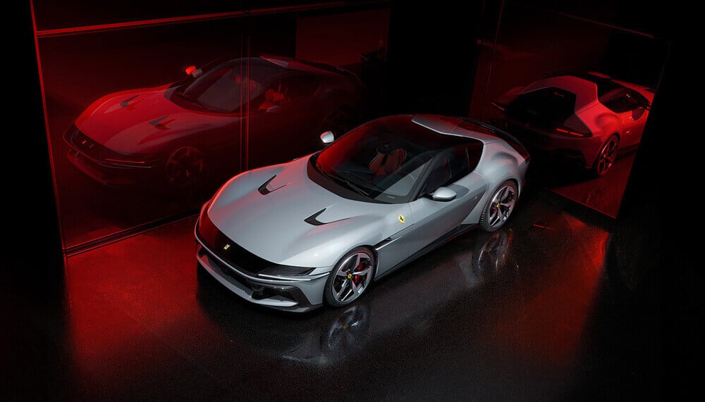 La imagen muestra un elegante coche deportivo plateado con un logotipo prominente en la parte frontal, indicando que es un Ferrari. El coche está posicionado en una habitación oscura con iluminación roja, y su reflejo es visible en las paredes de vidrio circundantes, creando un efecto dramático y visualmente impactante. El diseño del coche presenta líneas afiladas, curvas aerodinámicas y un perfil bajo, enfatizando sus capacidades de alto rendimiento. Esta imagen es interesante y relevante ya que destaca la naturaleza lujosa y poderosa de la marca Ferrari, enfocándose particularmente en el modelo de motor de 12 cilindros, conocido por su rendimiento excepcional y excelencia en ingeniería.