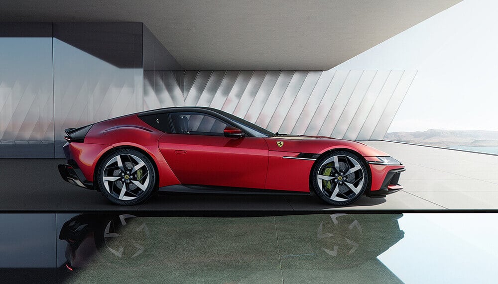 "La imagen muestra un elegante coche deportivo rojo, específicamente un Ferrari 12 Cilindri, estacionado en un entorno moderno y minimalista. El coche tiene un perfil bajo, un diseño aerodinámico y grandes ruedas de aleación estilizadas. Al fondo, se puede ver una estructura arquitectónica contemporánea con elementos de vidrio y metal, que reflejan la imagen del coche. El diseño del coche y el entorno sugieren un vehículo de alta gama y lujo, de gran interés para los entusiastas de los coches y aquellos interesados en el diseño automotriz moderno.