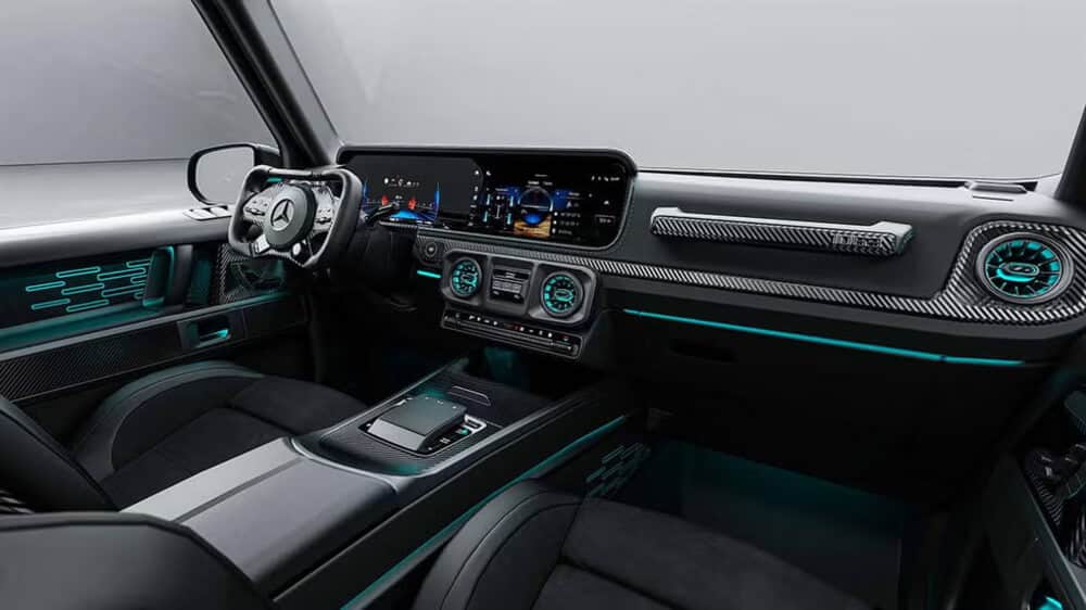 Interior del HOF Sir Class, un Mercedes-Benz Clase G modificado, con acabados en fibra de carbono, iluminación azul Petronas y un volante cuadrado inspirado en la Fórmula 1. El diseño combina lujo y deportividad con tecnología avanzada en las pantallas digitales.