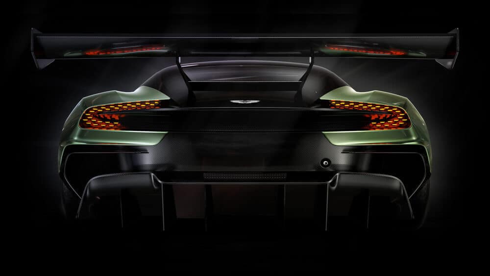 La imagen muestra la vista trasera de un Aston Martin Vulcan. El coche cuenta con un gran alerón trasero, un diseño intrincado de las luces traseras con múltiples elementos LED y un difusor trasero prominente, lo que indica su enfoque en la aerodinámica y la estabilidad a alta velocidad. La carrocería del coche parece estar hecha de fibra de carbono, lo que añade a sus características de ligereza y alto rendimiento. Esta imagen es interesante y relevante ya que destaca el diseño avanzado y la ingeniería que se invierten en la creación de coches deportivos de alto rendimiento.