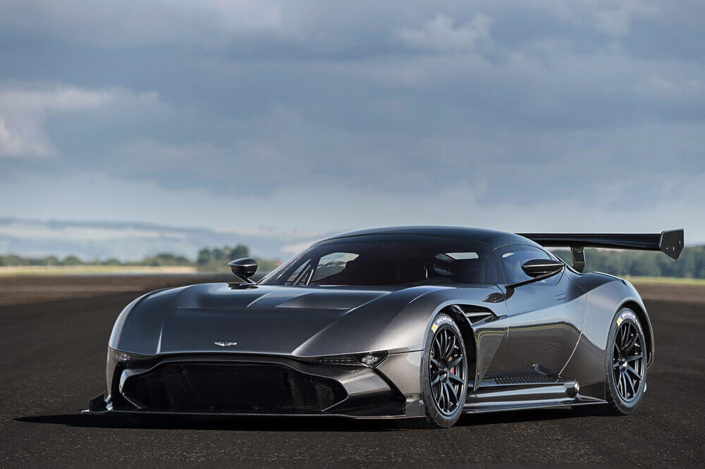 La imagen muestra un Aston Martin Vulcan de alto rendimiento en una pista de carreras. El coche tiene un diseño aerodinámico con un gran alerón trasero, lo que indica que está construido para la velocidad y el manejo. La carrocería es de color gris metálico y presenta un estilo agresivo con líneas afiladas y grandes tomas de aire. Esta imagen es interesante y relevante porque muestra un coche deportivo moderno y de alta gama, probablemente diseñado para carreras o para entusiastas de la conducción a alta velocidad.