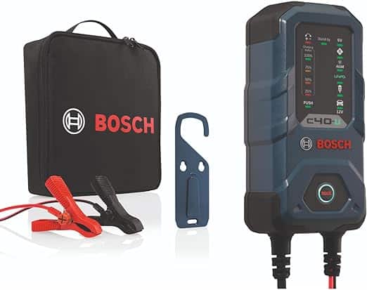 La imagen muestra un kit de cargador de batería Bosch C40. El kit incluye un estuche de transporte negro con el logotipo y nombre de Bosch en rojo, un par de pinzas de batería rojas y negras, un soporte de montaje azul y la unidad principal del cargador de batería. La unidad del cargador tiene una pantalla digital con varios indicadores como "Stand By," "6V," "12V," "LiFePO4," y "Push." El cargador está diseñado para cargar y mantener diferentes tipos de baterías, lo que lo hace relevante para aplicaciones automotrices y otras aplicaciones que utilizan baterías.