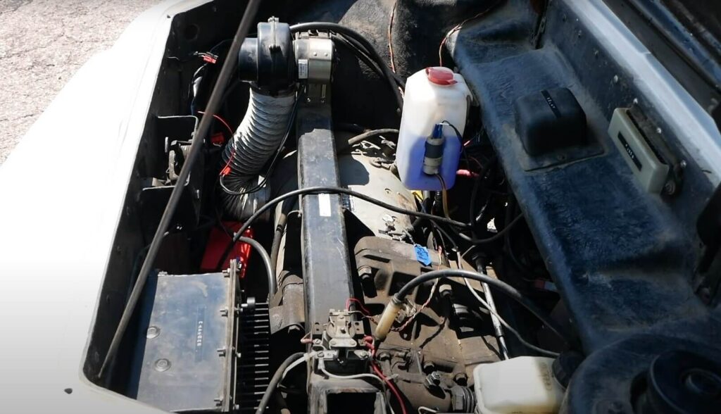 "Imagen del compartimento del motor del Electrek UNCAR, un coche eléctrico único de 1979 fabricado por Unique Mobility. La imagen muestra un motor eléctrico, varios cables, una batería y un depósito de refrigerante. La presencia de estos componentes sugiere que el vehículo ha sido convertido de un motor de combustión interna tradicional a un sistema de propulsión eléctrica. Esta conversión destaca la tendencia creciente y la viabilidad de transformar vehículos existentes a energía eléctrica, contribuyendo a soluciones de transporte sostenibles.