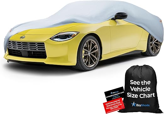 La imagen muestra un coche deportivo amarillo parcialmente cubierto por una funda de color claro. El coche está posicionado en un ángulo que muestra su parte frontal y lateral. Al lado del coche, hay una bolsa negra con cordón con el texto "See the Vehicle Size Chart" y el logo "EzyShade." Además, hay dos tarjetas, una negra y una roja, con el texto "CUSTOMER WARRANTY CARD" y "CUSTOMER KIT" respectivamente. Esta imagen es interesante y relevante ya que destaca un producto de funda para coche, demostrando su ajuste y los accesorios incluidos.