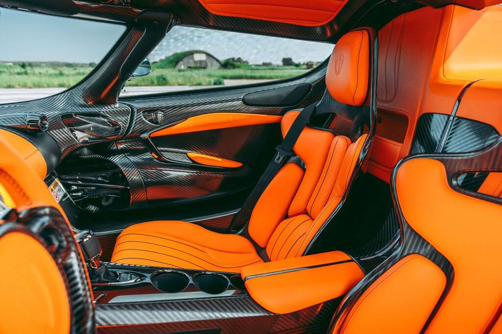 Gracias por la corrección. La imagen muestra el interior de un Koenigsegg Jesko. Los asientos y los paneles interiores están tapizados en cuero naranja brillante, y hay numerosos detalles en fibra de carbono en todo el habitáculo. El diseño es elegante y moderno, con un enfoque en el lujo y el rendimiento. Esta imagen es interesante porque destaca el uso de materiales premium y el diseño avanzado en interiores automotrices, mostrando la combinación de estética y funcionalidad en vehículos de alto rendimiento.