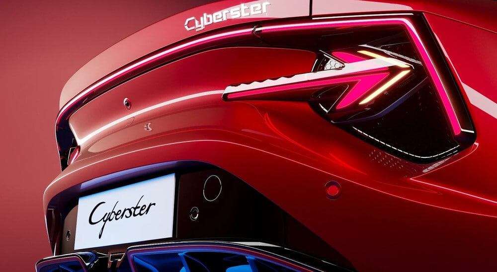 "El extremo trasero de un MG Cyberster rojo con el nombre 'Cyberster' mostrado prominentemente en la parte trasera. El diseño presenta líneas modernas y elegantes con luces traseras angulares distintivas que tienen una apariencia futurista. El nombre del coche también se muestra en el área de la matrícula. La iluminación y los reflejos en la superficie del coche resaltan su acabado brillante y diseño aerodinámico.