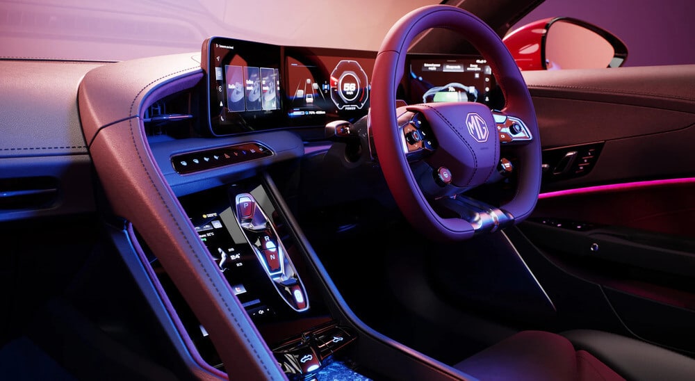 El interior de un coche moderno, específicamente enfocado en el lado del conductor. El volante presenta el logotipo de MG y hay múltiples pantallas digitales en el tablero. La consola central tiene una pantalla táctil con controles de cambio de marcha etiquetados como P, R, N y D. El tablero muestra información variada, incluyendo la velocidad y otros parámetros del vehículo. El diseño interior es elegante y futurista, con iluminación ambiental y una combinación de materiales de cuero y alta tecnología.