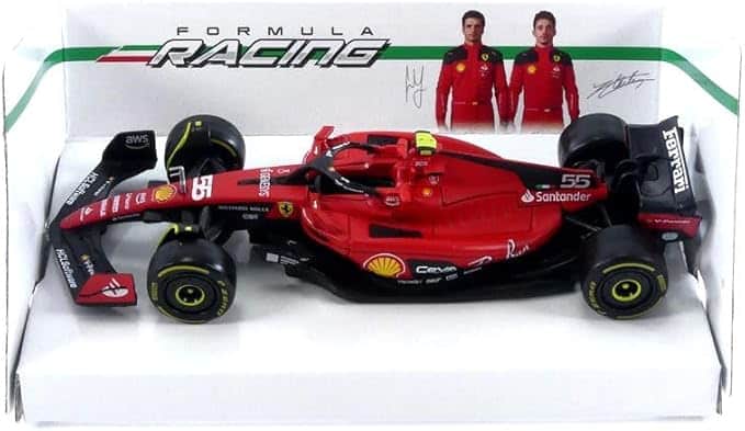La imagen muestra un modelo de coche de carreras de Fórmula 1 en una caja de exhibición, representando a Carlos Sainz y Charles Leclerc de Ferrari. El coche es predominantemente rojo con detalles en negro y amarillo, y lleva el número 55 en el morro y los laterales. Tiene varios logotipos de patrocinadores, incluyendo Shell, Santander y Pirelli. La caja de exhibición tiene el texto "FORMULA RACING" en la parte superior, junto con imágenes de los dos pilotos con trajes rojos. Este modelo es detallado y parece ser un artículo de colección, probablemente de interés para los fanáticos de la Fórmula 1 o coleccionistas de coches en miniatura. Si haces clic en la imagen, te lleva a Amazon para comprarlo.