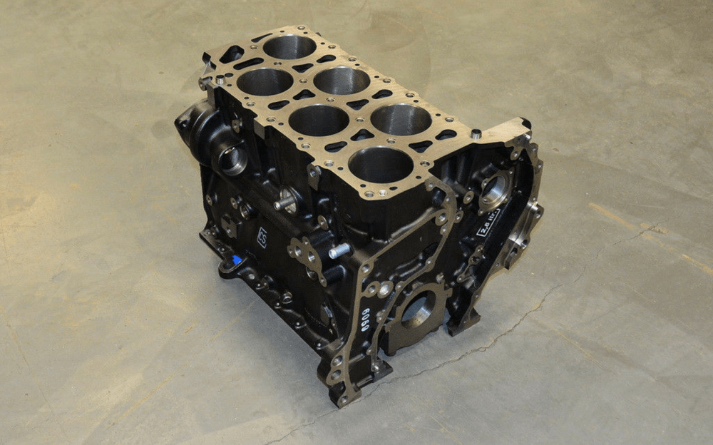 Esta imagen muestra un bloque de motor, que es un componente crucial de un motor de combustión interna. El bloque del motor alberga los cilindros y otras partes del motor, como el cigüeñal y el árbol de levas. Este bloque de motor en particular parece tener una configuración VR6, como lo indican los seis cilindros visibles en la superficie superior. El bloque del motor es interesante y relevante porque es la base de la estructura del motor y juega un papel vital en el rendimiento y la durabilidad del motor.