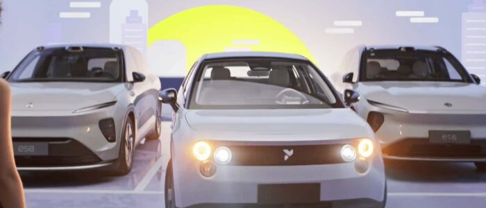 Tres vehículos eléctricos NIO estacionados en fila. El vehículo en el centro tiene los faros encendidos, y los vehículos a ambos lados tienen un diseño moderno y elegante. El fondo presenta un paisaje urbano estilizado con un gran sol o luna amarilla, añadiendo un tema futurista y de energía limpia a la escena. Los vehículos a la izquierda y derecha tienen la designación del modelo 'ES8' visible en sus matrículas delanteras. Esta imagen es interesante y relevante ya que destaca el avance y la promoción de los vehículos eléctricos, cruciales para el transporte sostenible y la reducción de emisiones de carbono.