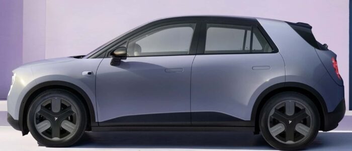 Vista lateral de un NIO Firefly, un coche eléctrico compacto, conduciendo por una carretera. El vehículo tiene un diseño moderno y elegante con líneas aerodinámicas y un acabado metálico brillante. El fondo muestra un paisaje urbano con edificios altos y un cielo despejado. Esta imagen es interesante y relevante ya que destaca el diseño y la funcionalidad del NIO Firefly, subrayando su atractivo como opción de transporte sostenible en entornos urbanos.