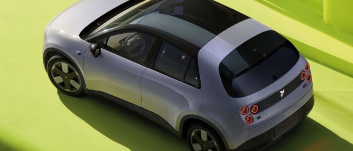 Un vehículo eléctrico compacto NIO Firefly con un diseño moderno y elegante. El coche tiene una carrocería plateada con un techo negro y ruedas grandes y estilizadas. La parte trasera del coche presenta luces traseras circulares distintivas y un logotipo en el centro. El coche está estacionado sobre una superficie verde brillante, lo que contrasta con el color del coche y resalta su diseño. Esta imagen es interesante porque muestra un vehículo eléctrico contemporáneo, enfatizando su atractivo estético y su naturaleza ecológica.