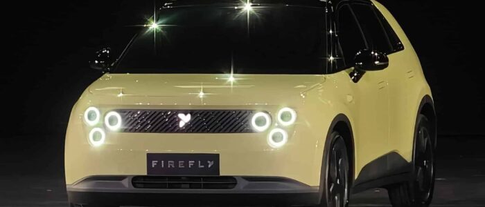 Un vehículo eléctrico compacto NIO Firefly de color amarillo con un diseño moderno y minimalista. El frontal del coche presenta faros LED circulares dispuestos en pares a cada lado y una parrilla con un pequeño logotipo iluminado en el centro. La matrícula muestra el nombre 'FIREFLY'. El coche tiene una apariencia elegante y futurista, destacando su naturaleza eléctrica y su diseño innovador.