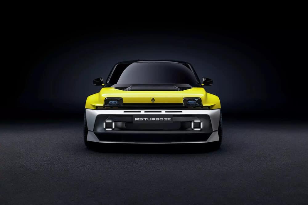 La imagen muestra la vista frontal de un coche deportivo moderno con un diseño distintivo. El coche tiene un color amarillo brillante en la parte superior y un color plateado en la parte inferior. Los faros son rectangulares con un aspecto elegante y futurista, y hay luces adicionales integradas en el parachoques delantero. El coche tiene una insignia en el centro de la parrilla frontal y el texto 'R5 TURBO 3E' se muestra de manera prominente en el parachoques delantero. Esta imagen es interesante porque muestra un diseño de coche único y moderno, probablemente un concepto o un modelo de edición especial, que puede atraer a los entusiastas de los coches y a aquellos interesados en el diseño automotriz.